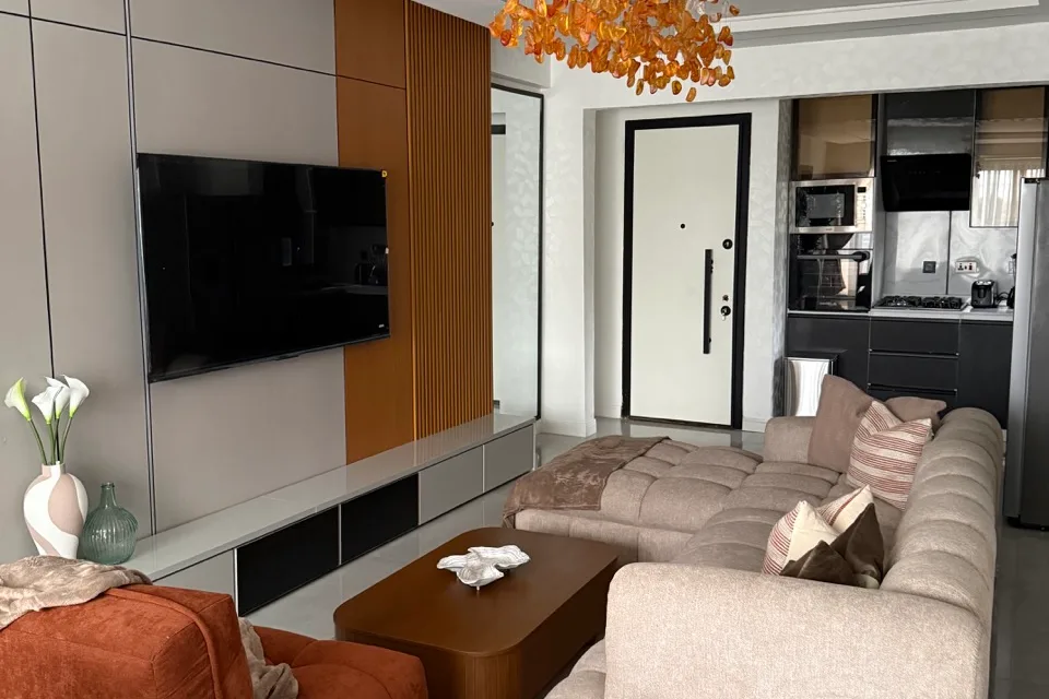 The living room at Daisy, Urban Pumpkin's two bedroom apartment in Ikoyi, with a cream corner sofa, a burnt orange armchair and an amber glass chandelier