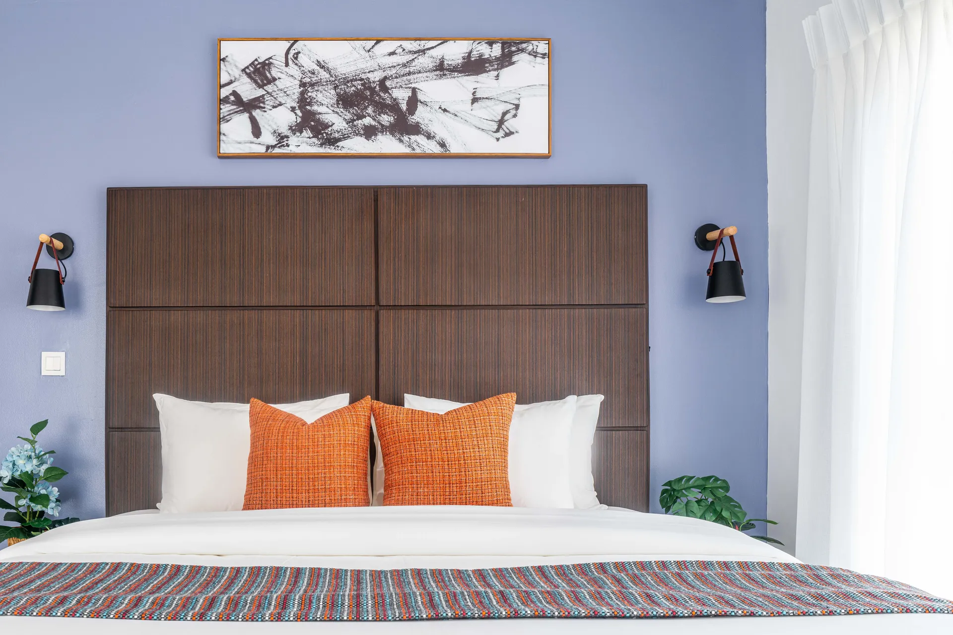 A king bedroom in an Urban Pumpkin apartment in Lagos: a tall wood panel headboard, crisp white bedding and burnt orange cushions