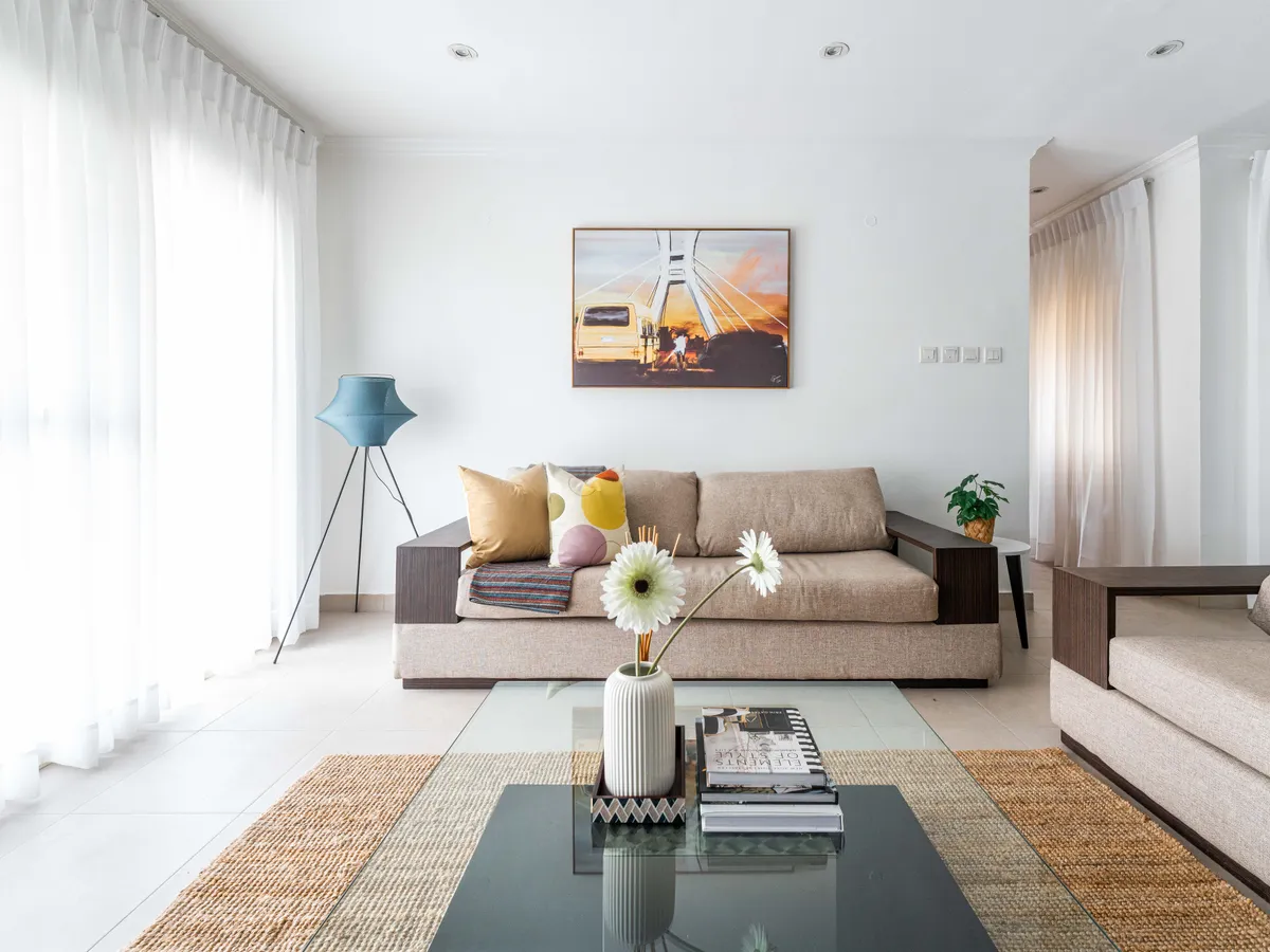 A bright living room in an Urban Pumpkin apartment, with a painting of a Lagos danfo bus crossing the Lekki-Ikoyi bridge above the sofa